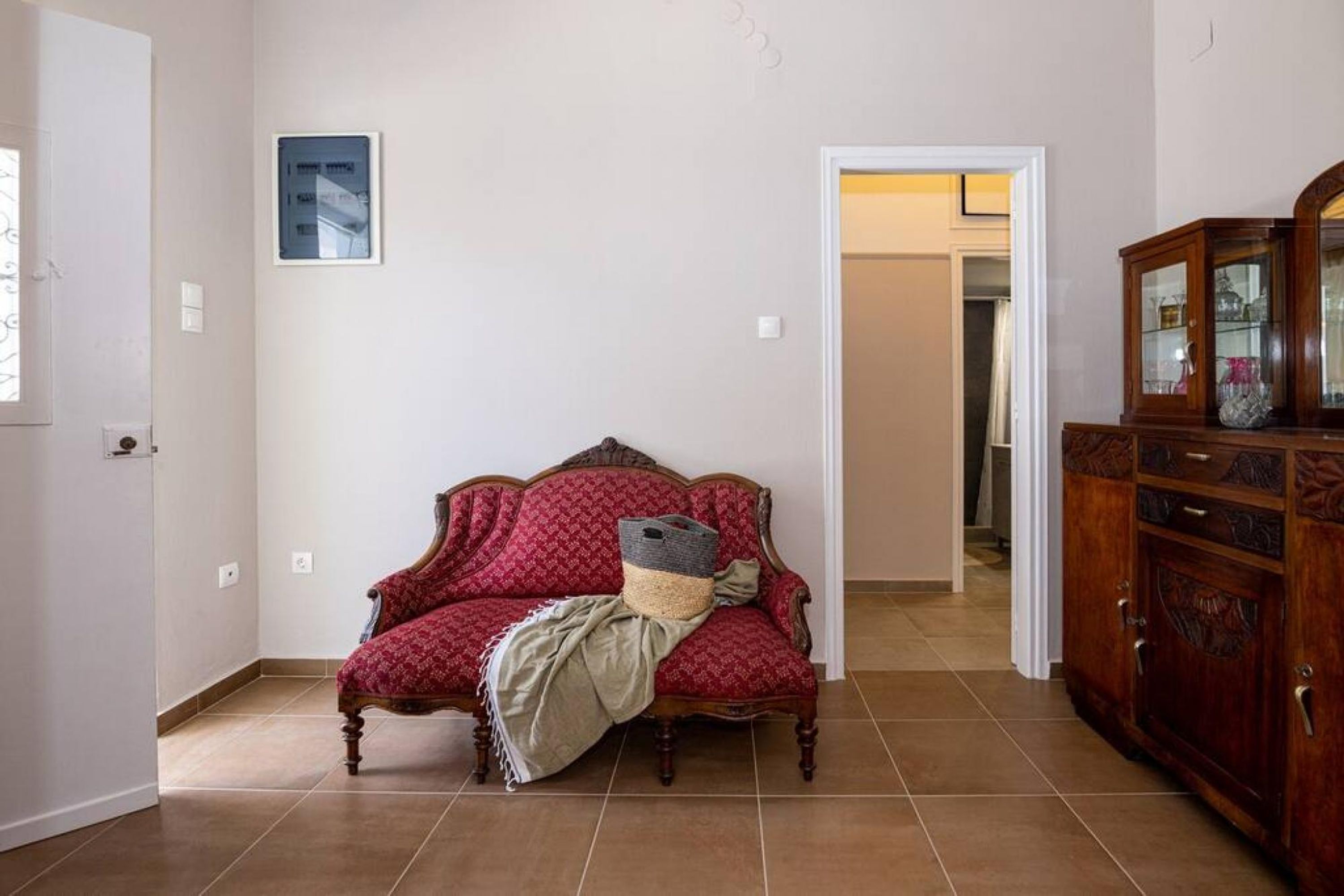 Una habitación con un sofá rojo estampado, un mueble de madera con puertas de cristal y un cuadro en la pared.