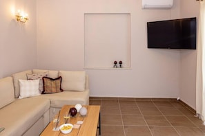 A living room with a sofa, a coffee table with snacks, a flat-screen TV mounted on the wall, and a wall-mounted air conditioner. - Mellow Mood Tinos Town (Tinos)