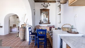 A rustic kitchen with a wooden table, blue chairs, a hanging chandelier, and a large vase. - Daphnis the Artist s House (Tinos)
