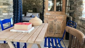 A rustic room with a wooden table, blue chairs, a bed with white bedding, and a wooden cabinet with glass doors. - Delphis the Artist s House (Tinos)