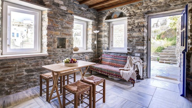 A stone-walled room with a wooden table, chairs, and a colorful sofa. - Delphis the Artist s House (Tinos)