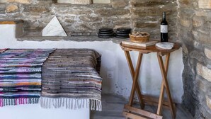 A rustic room with a stone wall, a wooden bench, a small table with a bottle, and a hanging light fixture. - Delphis the Artist s House (Tinos)