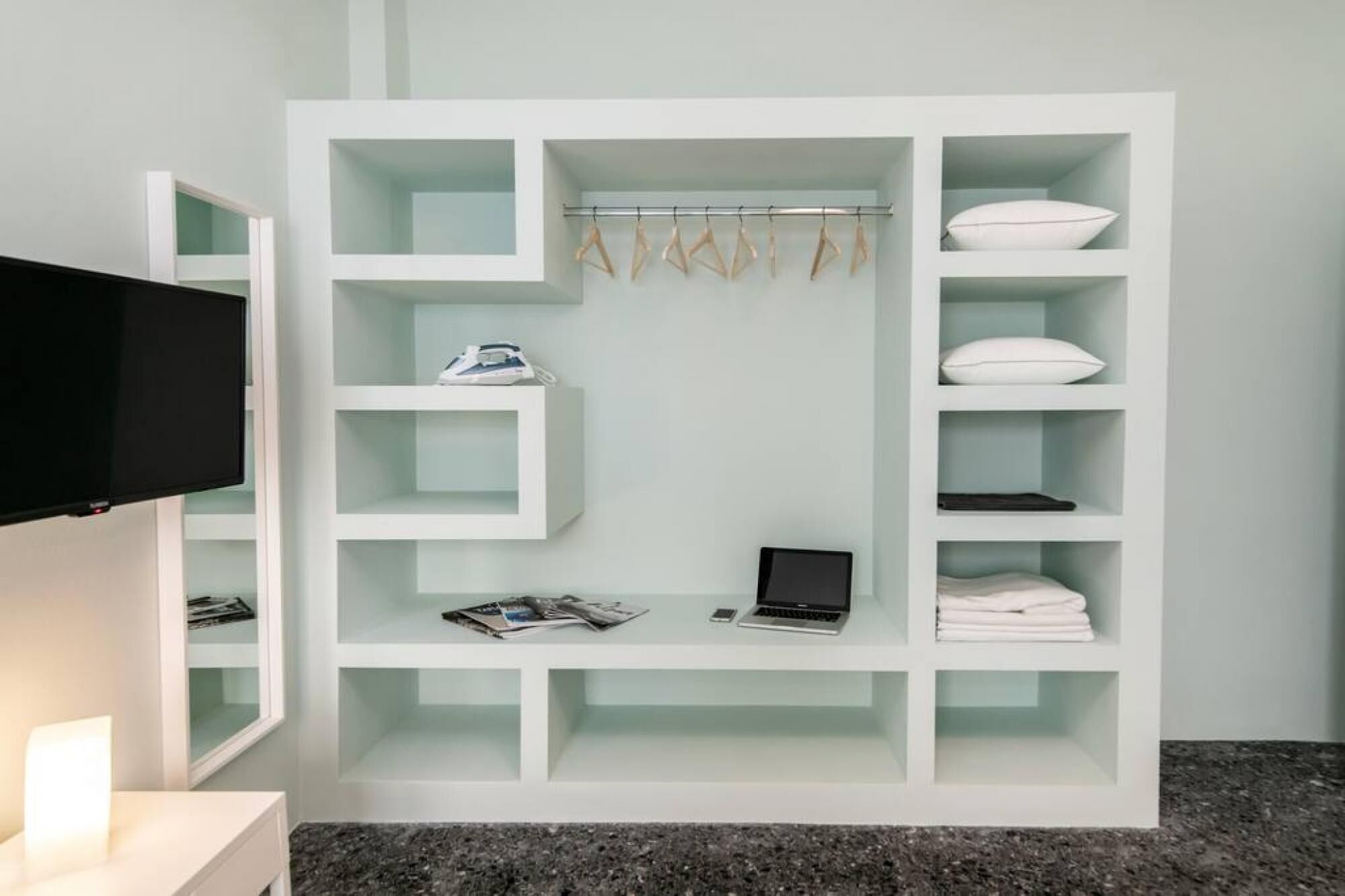 A modern, white storage unit with multiple compartments, including shelves for clothing, a laptop, and a shoe rack.