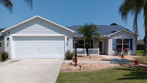 A two-story house with a garage, a front porch, and a small garden area. - Paradise Village home in perfect golfing and recreation center location.  (The Villages)