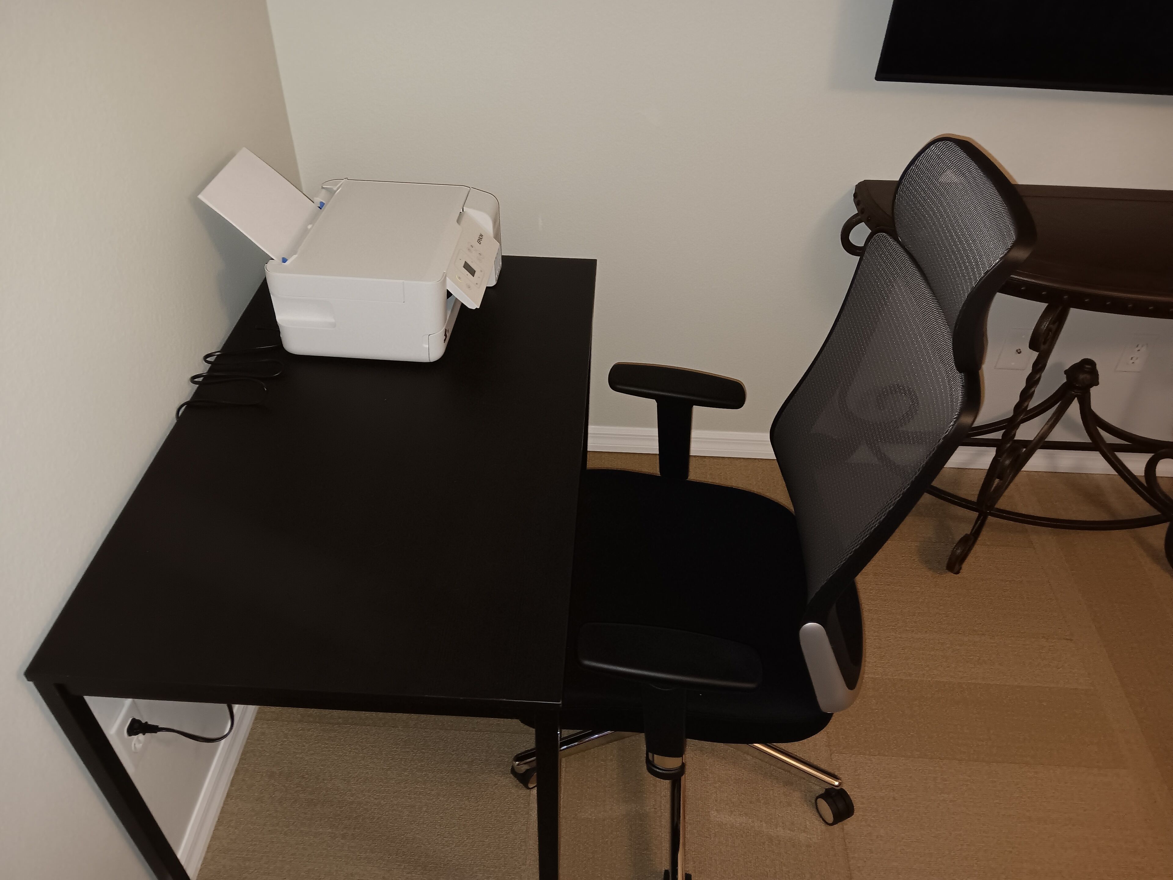 A black desk with a printer, a black office chair, and a small table with a chair.