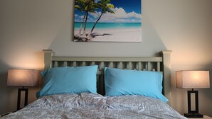 A bed with a white textured bedspread, two light blue pillows, and a painting of a beach scene above it. - Paradise Village home in perfect golfing and recreation center location.  (The Villages)