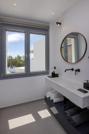 Ein modernes Badezimmer mit großem Fenster, rundem Spiegel und integriertem Waschbecken.