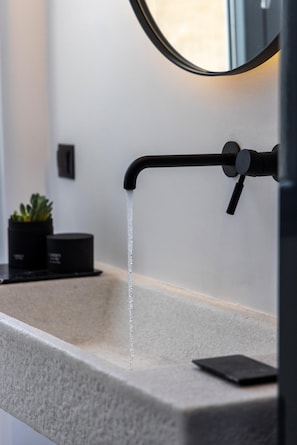 Ein modernes Badezimmer mit einem eleganten schwarzen Wasserhahn, einem runden Spiegel und einem kleinen Topfpflanzen auf der Ablagefläche.