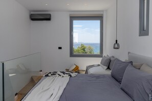 Ein modernes Schlafzimmer mit einem großen Bett, Meerblick und einer Glasreling.