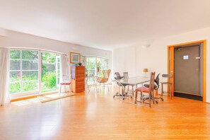 A spacious room with a large window, a wooden floor, a desk with chairs, and a door.