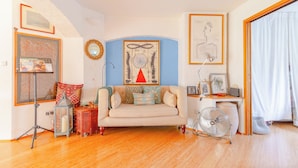 A living room with a sofa, a standing lamp, a framed artwork, and a fan. - Uniquely Designed 2BD Flat near Tower Bridge (London)