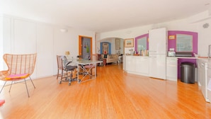 A modern kitchen with a white refrigerator, a sink, and a countertop. There is a dining area with a table and chairs. - Uniquely Designed 2BD Flat near Tower Bridge (London)