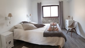Ein Schlafzimmer mit Bett, Nachttischen, einem Sessel, einem Fenster mit Vorhängen und einer Steinwand.