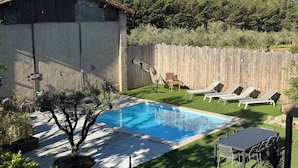 Ein Garten mit Schwimmbecken, Holzpforte und einem kleinen Gebäude.