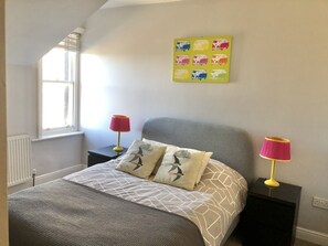 A bedroom with a bed, two bedside tables, a window, and a wall art piece. - Charming and spacious Victorian townhouse (Harrogate)