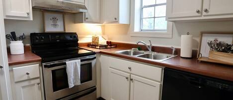 A kitchen with white cabinets, a black stove, a sink, and a window.