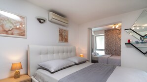 A modern bedroom with a large bed, bedside tables, a wall-mounted air conditioner, and artwork.