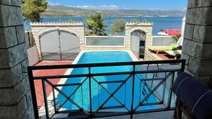 A stone archway leading to a pool area with a view of the sea and distant mountains.
