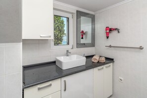 Een moderne badkamer met een wit wastafelmeubel, een spiegel met decoratieve lijst, een handdoekhouder en een raam met uitzicht op bomen.