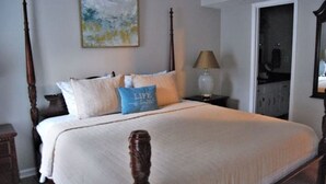 A bedroom with a four-poster bed, a bedside table, a lamp, and a painting on the wall.