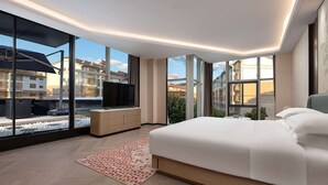 A modern bedroom with a large bed, a TV, and a view of the city through large windows. - Ramada by Wyndham Honghe Kaiyuan (Honghe)