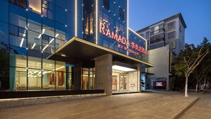 A modern hotel with a glass facade, a prominent sign reading "RAMADA BY WYNDHAM," and a well-lit entrance area. - Ramada by Wyndham Honghe Kaiyuan (Honghe)