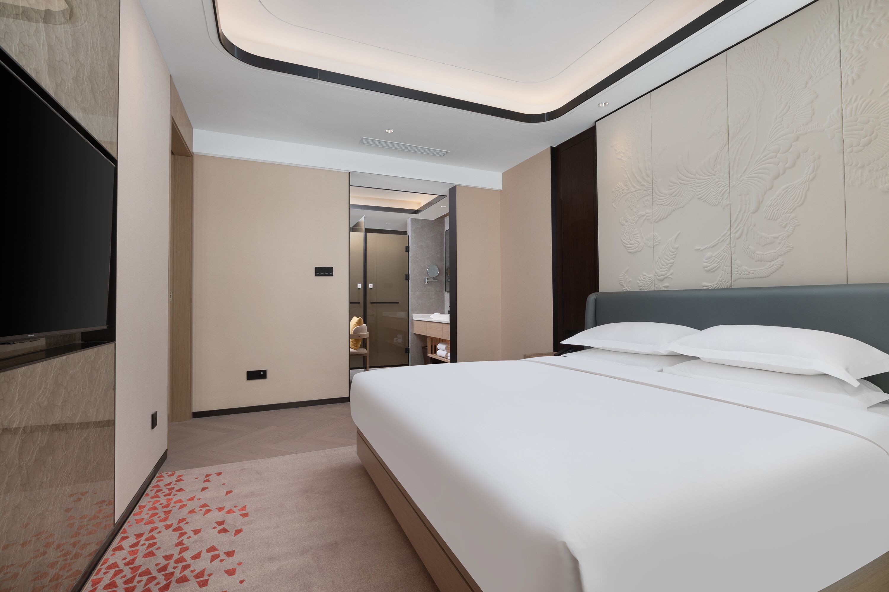 Camera d'albergo moderna con un letto grande, una televisione a schermo piatto e un bagno visibile attraverso una porta aperta.