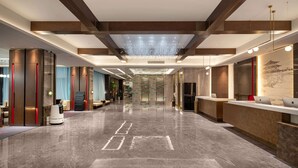 A spacious lobby with a high ceiling, a reception desk, and a robot. - Ramada by Wyndham Honghe Kaiyuan (Honghe)