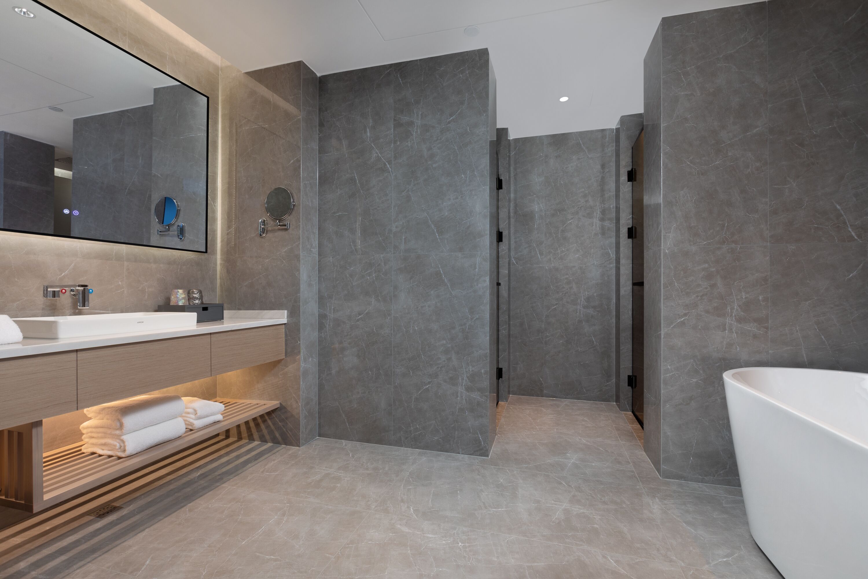 A modern bathroom with a large mirror, a sink, a bathtub, and a vanity with towels.