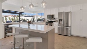 A modern kitchen with white cabinets, stainless steel appliances, a large island with bar stools, and pendant lighting. - 10 Bd/walk 2 shuttle 4 Stagecoach/Ask-Deals/Games (La Quinta)