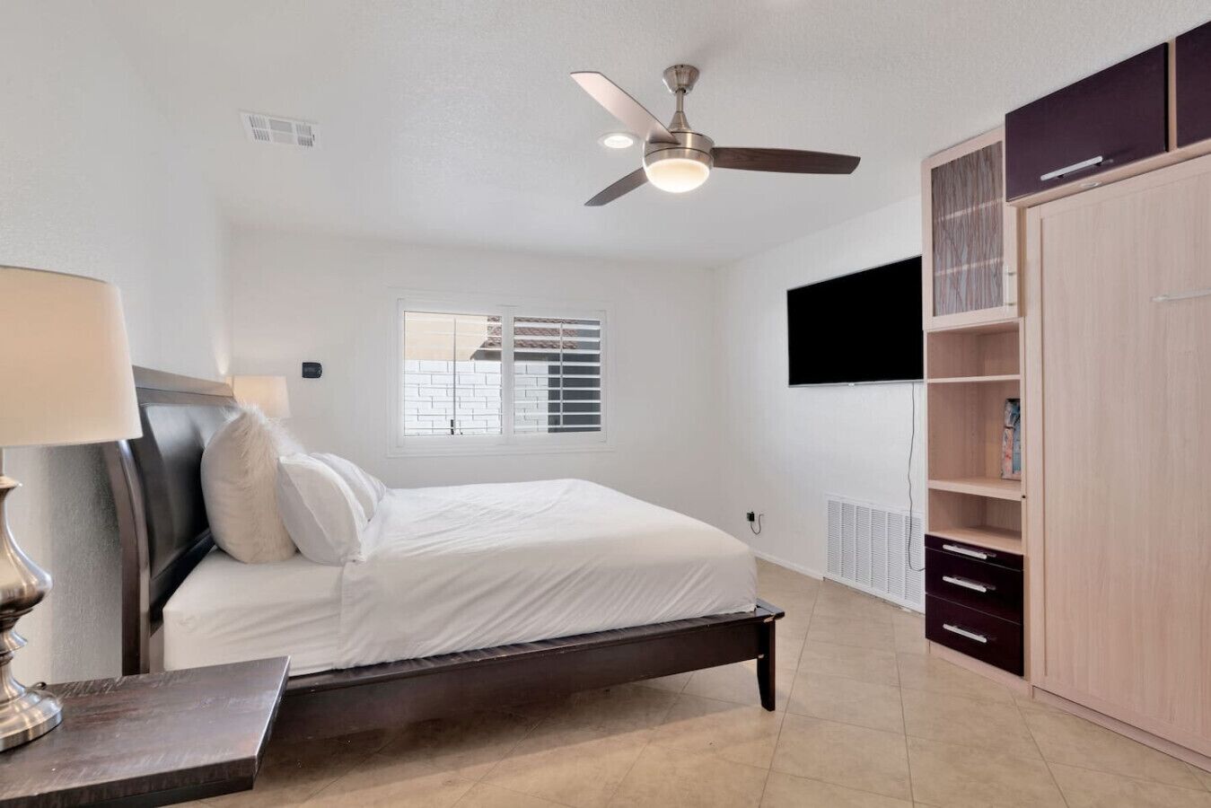 A bedroom with a bed, a ceiling fan, a TV mounted on the wall, and a wardrobe.