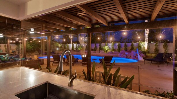A modern kitchen with a stainless steel sink, a wooden ceiling, and a view of an outdoor pool area with seating and plants. - 10 Bd/walk 2 shuttle 4 Stagecoach/Ask-Deals/Games (La Quinta)