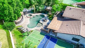 Une propriété résidentielle dotée d’une piscine, d’un court de tennis et d’une végétation luxuriante.
