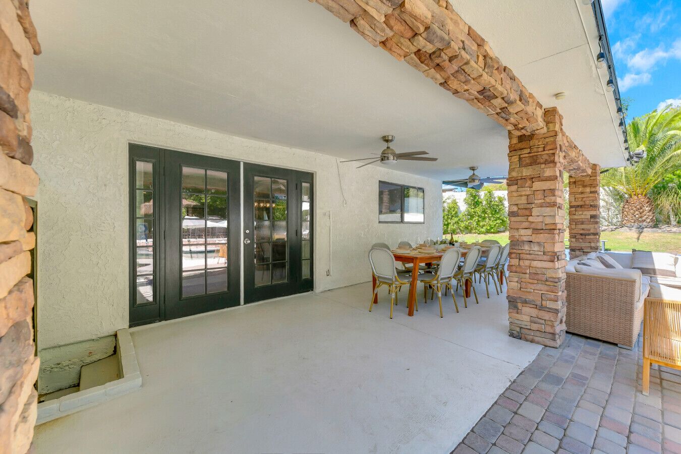 A covered patio area with a dining table and chairs, a ceiling fan, and a stone archway.