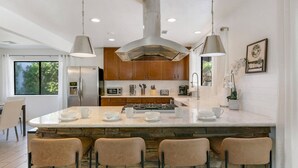 Une cuisine moderne dotée d’un îlot central, de tabourets de bar et de luminaires suspendus.