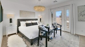 Une chambre avec un grand lit, deux tables de chevet, un lustre, une vue sur l’extérieur par une porte coulissante et un tapis.