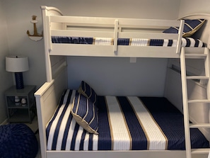 Una cama litera con ropa de cama a rayas, una mesita de noche con lámpara y un ancla decorativa en la pared.
