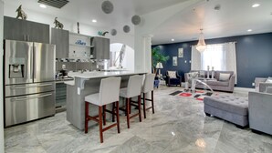 Een moderne keuken met een bar, een eethoek met barstoelen, en een zithoek met een bank en poef.