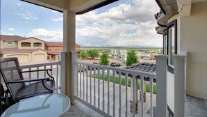 Een balkon met een glazen tafel en stoelen, met uitzicht op een buitenwijk met huizen en een heldere lucht.