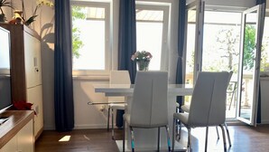 Un comedor moderno con una mesa y sillas blancas, un armario de madera y un televisor a la izquierda.