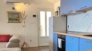 Una cocina moderna con armarios azules, horno empotrado y microondas. El suelo es de madera y hay una puerta que da a otra habitación.