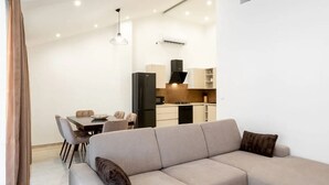 Un salon moderne avec un canapé d’angle beige, un coin repas comprenant une table et des chaises, et une cuisine en arrière-plan.