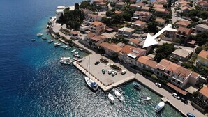 Vue aérienne d’une ville côtière avec un port de plaisance, des maisons à étages et un imposant bâtiment blanc.