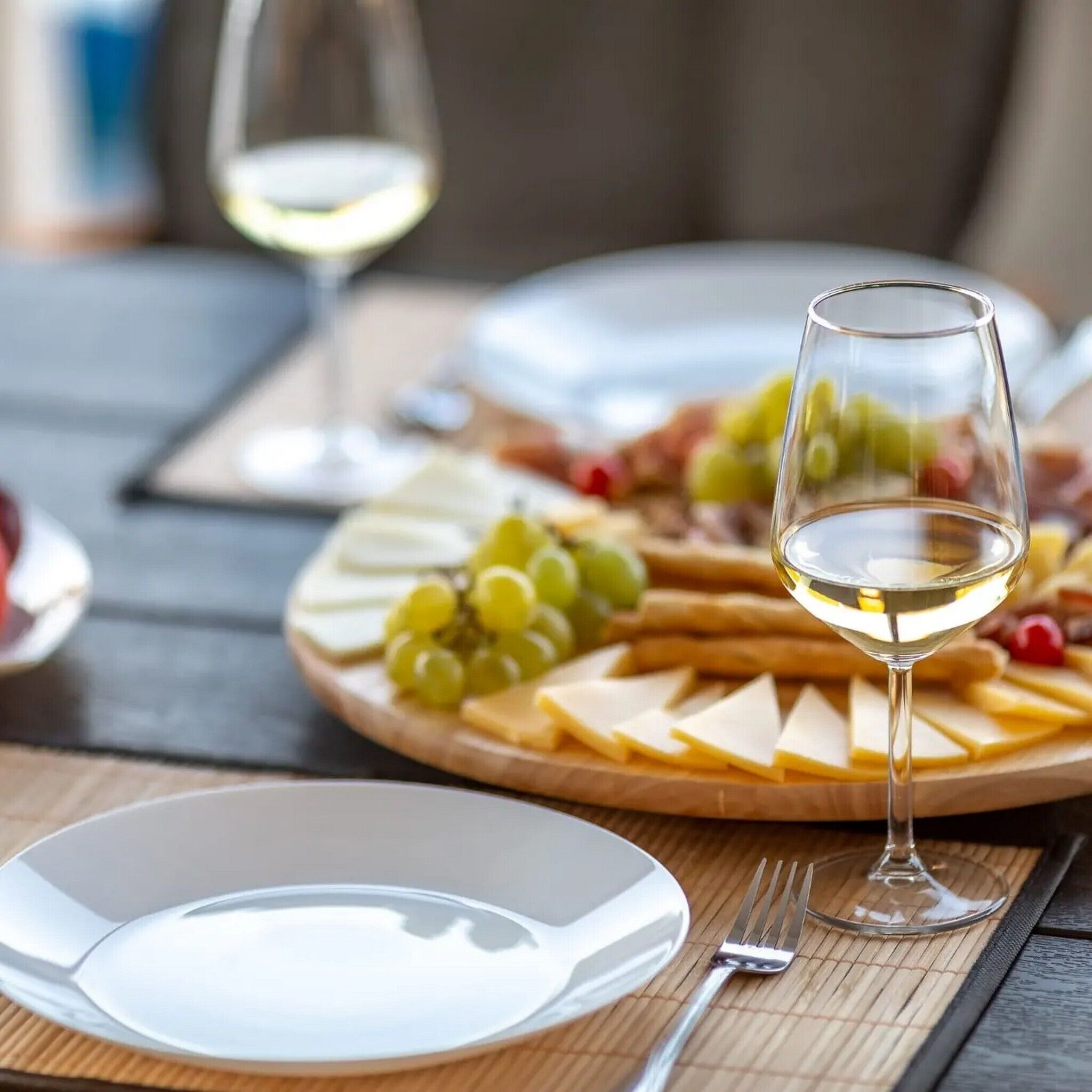 Ein Tisch mit Käseplatte, Trauben und einem Glas Weißwein.