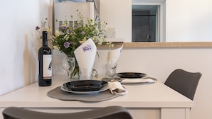 A dining table set with plates, glasses, a wine bottle, and a vase with flowers. - Apartments Roza - Studio Apartment (Mlini)