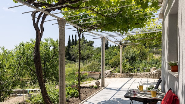 A covered patio with a table and chairs, surrounded by greenery and a pergola. - Apartments Roza - Studio Apartment (Mlini)