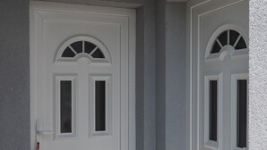 Eine weiße Tür mit kleinem Fenster und einem dekorativen Bogen darüber, in eine strukturierte Wand eingelassen.