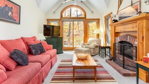 A cozy living room with a red sofa, a wooden coffee table, a fireplace, and a television. - Ski In Ski Out in style on Village Chair (Jay)