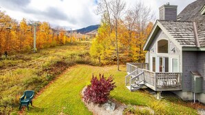 Ein Haus mit Veranda, Rasen und Herbstbäumen im Hintergrund.