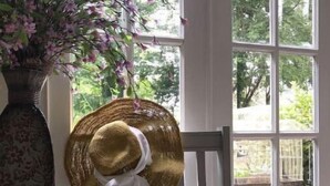 Ein Zimmer mit einem großen Fenster, einem hölzernen Stuhl und einem auf dem Stuhl hängenden Hut.